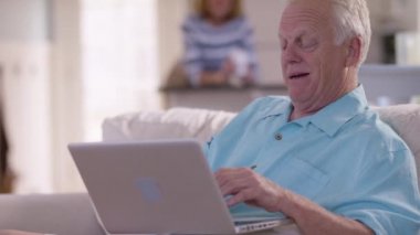 Oturma odasında dizüstü bilgisayar kullanan kıdemli bir adam.