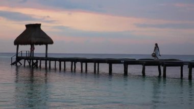 Kadın tropik tatil köyünde iskelede yürüyor.