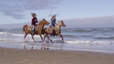 Kadınlar sahilde ağır çekimde ata biniyorlar.