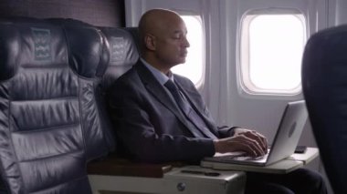 Uçakta dizüstü bilgisayar kullanan bir iş adamı