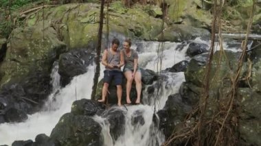 Hawaii 'de şelalenin yanında oturan çift.