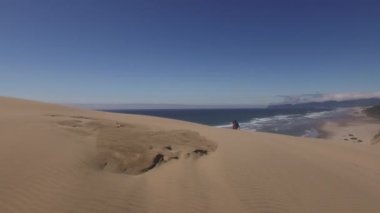 Kumsaldaki kum tepelerinde yürüyüş yapan çiftin hava görüntüsü.