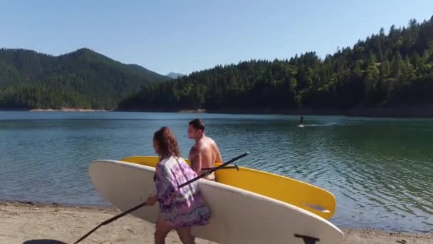 Paar Wandelen Bij Het Meer Met Stand Paddle Boards — Stockvideo