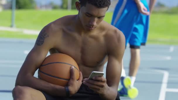 Tenåringsbasketballspiller Som Bruker Mobiltelefon Utendørs Bane – stockvideo