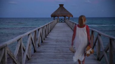 Bir kadın tropik tatil köyünde iskelede yürüyor.