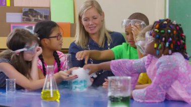 Öğretmen ve bir grup öğrenci okulda bir bilim deneyi yapıyor.