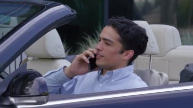 Genç işadamı cep telefonuyla konuşurken üstü açık arabaya biniyor.