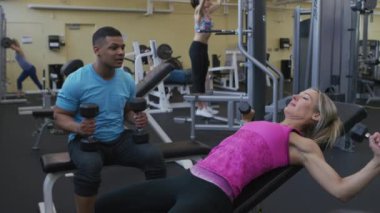 Spor salonunda kadın antrenörle ağırlık kaldırıyor.