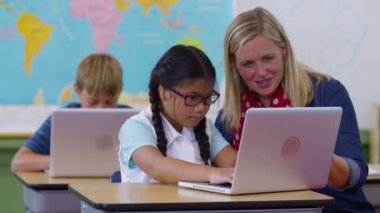 Öğretmen ve genç kız sınıfta dizüstü bilgisayar kullanıyor.