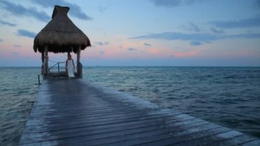 Bir kadın tropik tatil köyünde iskelede yürüyor.