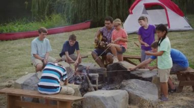 Yaz kampındaki çocuklar kamp ateşinde lokum kızartıyorlar.