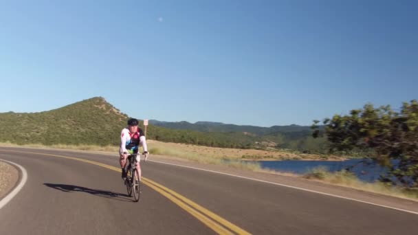人骑自行车在能俯瞰湖面的乡间路上 — 图库视频影像