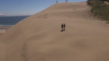 Kumsaldaki kum tepelerinde yürüyüş yapan çiftin hava görüntüsü.
