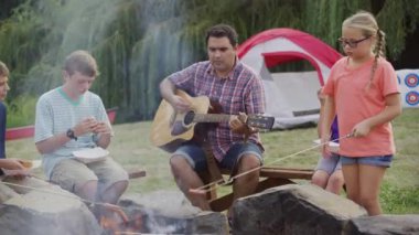 Kamptaki çocuklar kamp ateşinde gitar çalıyorlar.