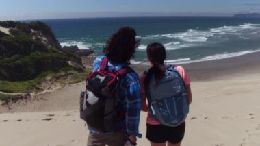 Kumsalda kum tepelerinde yürüyüş yapan bir çift manzaraya bakmak için mola verir.