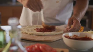 Şef pizzaya domates sosu sürer.