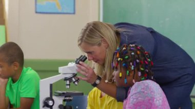 Öğretmen ve öğrenciler sınıftaki mikroskoplara bakıyorlar.