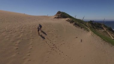 Kumsaldaki kum tepelerinde yürüyüş yapan çiftin hava görüntüsü.