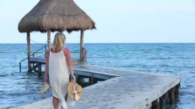 Bir kadın tropik tatil köyünde iskelede yürüyor.
