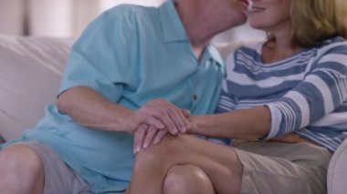 Kanepede birlikte oturan yaşlı çift sevgisini gösteriyor.