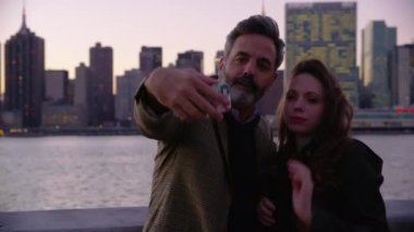 New York 'taki bir çift, arka planda gökyüzü olan cep telefonu selfie' si çekiyor.