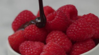 Kırmızı ahududular üzerine çikolata sosu dökülüyor. Kırmızı 8K kamerayla çekilmiş.