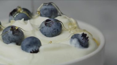 Yoğurt ve yaban mersininin üzerine bal serpiştirilmiş. Kırmızı 8K kamerayla çekilmiş.