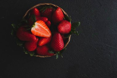Kasede taze çilekler, karanlık bir masanın üzerinde sade bir sahne..