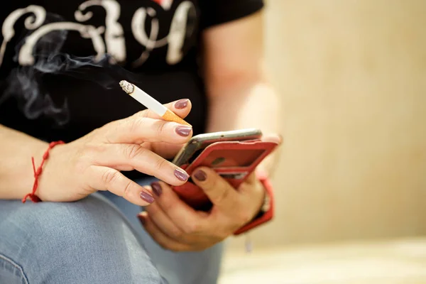 Kadın sigara içiyor ve akıllı telefonuna bakıyor.