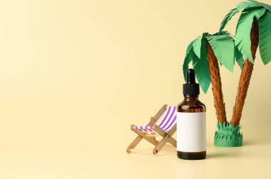 Kahverengi damlatan cam şişe ve şezlong palmiye ağacının altında sarı arka planda. Güneş banyosu sırasında cilt bakımı. Organik mineral kozmetik ürünü. Mockup, boşluğu kopyala