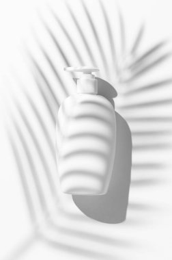 Beyaz arka planda palmiye yaprağı gölgesi olan plastik şişe. Yaz teni konsepti. Güneş kremi paketi. Üst görünüm