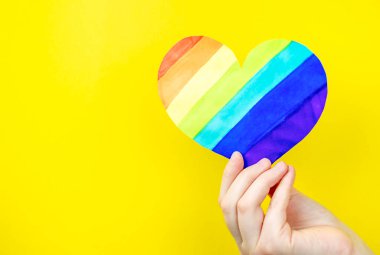 Sarı arka planda çok renkli kalbi tutan bir kadın. Aşk kavramı, LGBT
