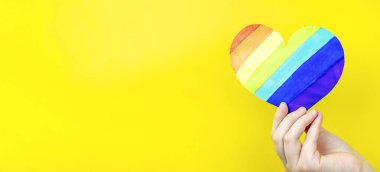 Sarı arka planda çok renkli kalbi tutan bir kadın. Aşk kavramı, LGBT