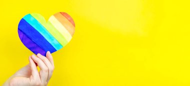 Sarı arka planda çok renkli kalbi tutan bir kadın. Aşk kavramı, LGBT