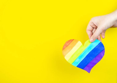 Sarı arka planda çok renkli kalbi tutan bir kadın. Aşk kavramı, LGBT