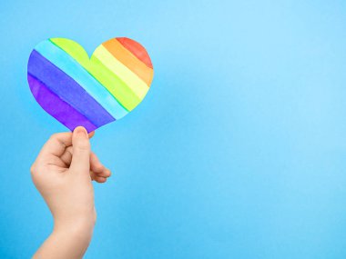 Mavi arka planda çok renkli kalbi tutan bir kadın. Aşk kavramı, LGBT