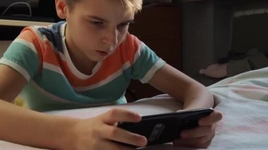 11 yaşında Avrupa görünümlü bir çocuk, evde telefonla oynuyor..