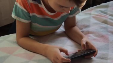 11 yaşında Avrupa görünümlü bir çocuk, evde telefonla oynuyor..
