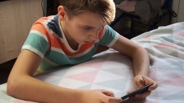 11 yaşında Avrupa görünümlü bir çocuk, evde telefonla oynuyor..