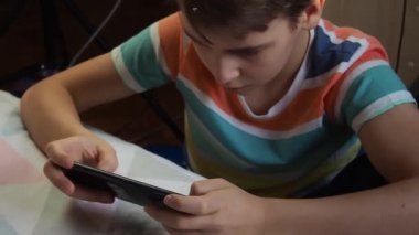 11 yaşında Avrupa görünümlü bir çocuk, evde telefonla oynuyor..