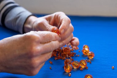 Evde boş zaman aktivitesi. Yaşlı bir kadının elleri turuncu mücevher yapıyor, bunama önleyici aktiviteler yapıyor.