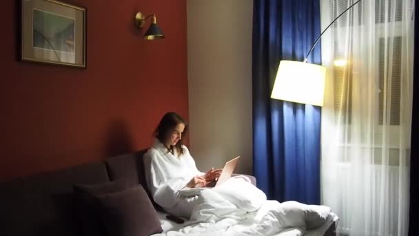 Zakelijke vrouw met een laptop in een hotelkamer gekleed in een badjas — Stockvideo