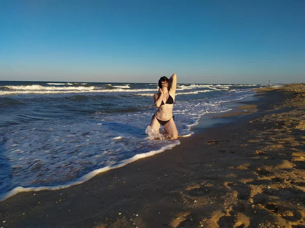 Joven mujer en traje de baño sentado en olas marinas cerca de la playa — Foto de Stock