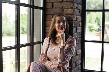 Pembe elbiseli güzel bir kadın pencere eşiğinde oturuyor. 