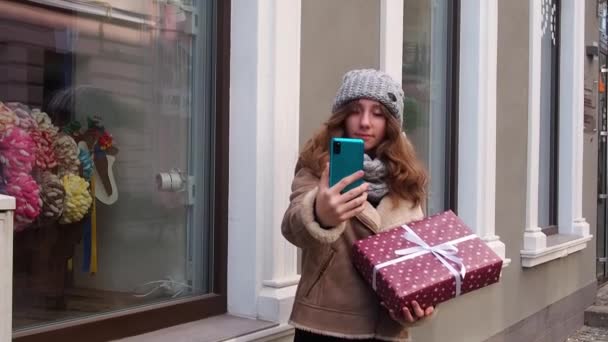 선물 상자로 셀카를 만드는 갈색 코트를 입은 소녀 — 비디오