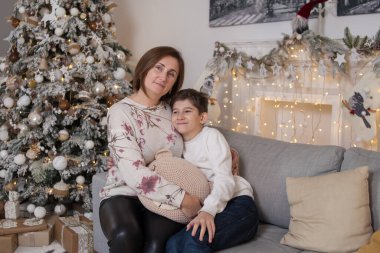 Mutlu anne ve oğul köknar ağacının yanındaki koltukta hediyelerle oturuyorlar.