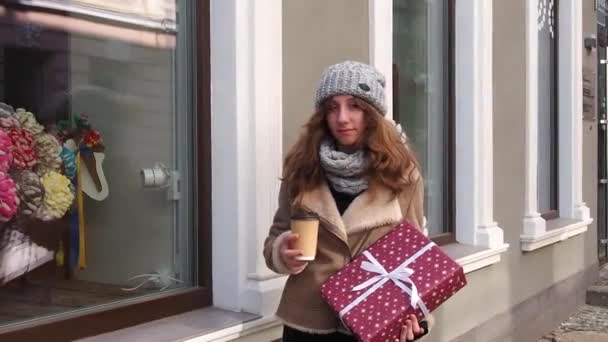 Flicka i en brun rock går ner på gatan med hämtmat kaffe — Stockvideo