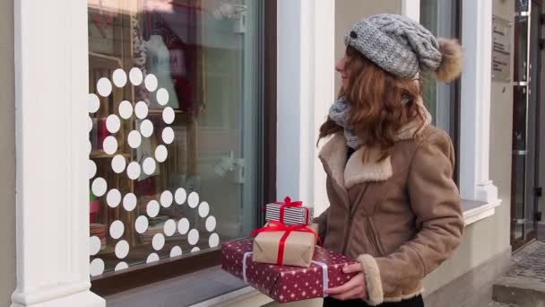 Teengirl sosteniendo un conjunto de regalos de Navidad cerca de la ventana de las tiendas — Vídeo de stock