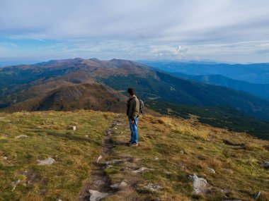 Dağın tepesinde duran adam dinleniyor ve güzel manzaranın tadını çıkarıyor.