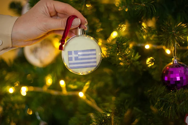 Une fille tient une décoration sur un arbre de Noël avec le drapeau de la Grèce — Photo